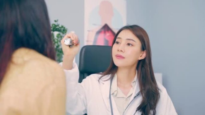 亚洲年轻女医生在医院用手电筒照病人的眼睛。迷人的专业医生戴着口罩，在诊所为女士检查视力。医疗保险服务