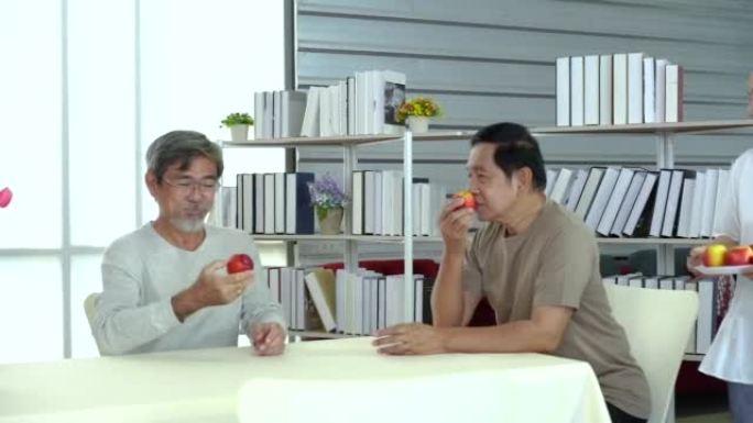 在房间里拿着苹果的亚洲人。一群吃红苹果的退休老人。一群学长在桌子上聊天。