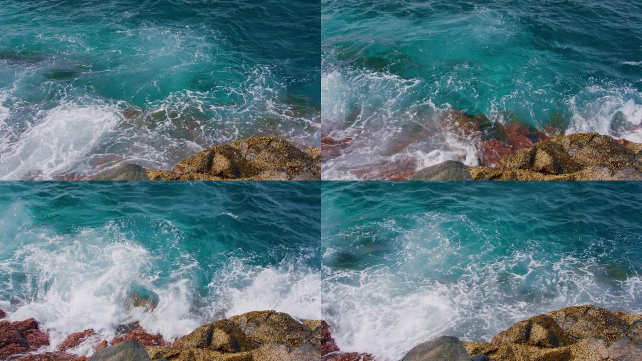 透明的蔚蓝水。特写，海浪在特内里费岛海滩上的湿石头上冲刷，阳光照在发泡水中