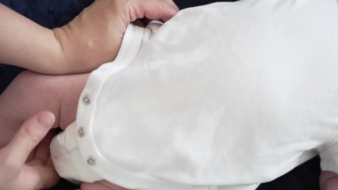 母亲的双手用白色连体衣打扮新生婴儿男婴的特写镜头