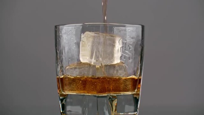 朗姆酒被倒入孤立的灰色背景上的冰玻璃杯中