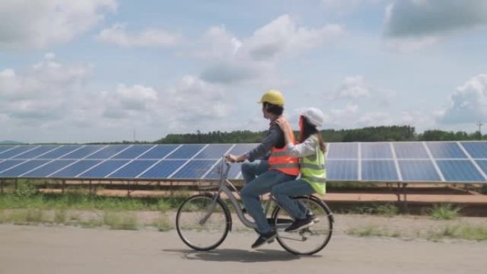 两名工人夫妇在太阳能农场骑自行车，并有乐趣检查太阳的运作和清洁光伏太阳能电池板。生态系统概念