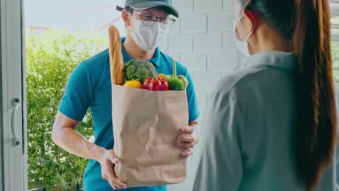 送餐概念。亚洲妇女手接受专业送货员邮递员和快递杂货递送的食品、水果、蔬菜袋