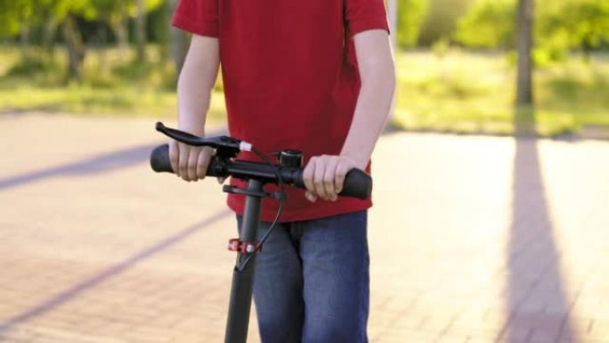 踢踏板车的孩子。夏天，小男孩在公园的小路上骑着踏板车。儿童休闲活动，运动