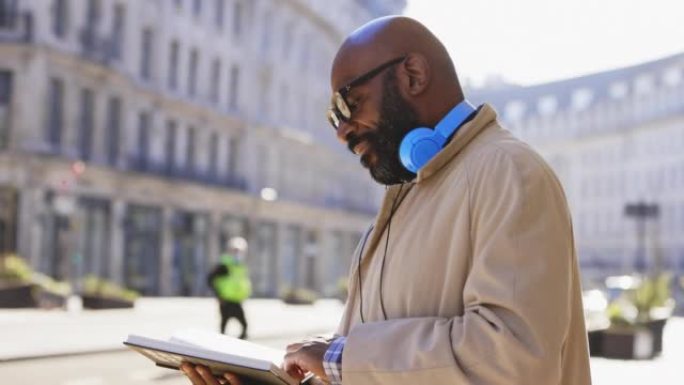阳光城市人行道上戴着耳机的成熟男人看书