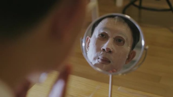 亚洲男子在脸上戴着面膜看着镜子时的倒影。