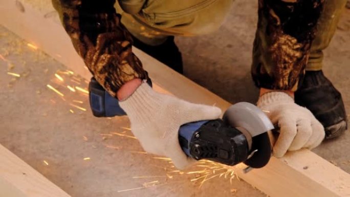 一名建筑商的双手戴着工作手套，用角磨机电动工具切割金属发夹。准备木地板的原木。亲手上门修理，锯木厂。
