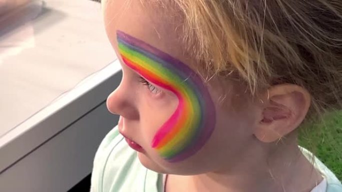 一个三岁女孩的特写。她的脸上涂有彩虹，上面涂有特殊的防水涂料aquagrim。