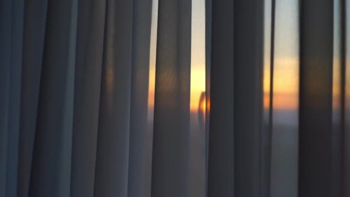摄像机在日落时沿着悬挂在窗户上的透明窗帘移动