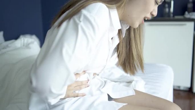 突然的女人有膀胱疼痛和胃痛坐在床上在卧室醒来后感到恶心和痛苦。