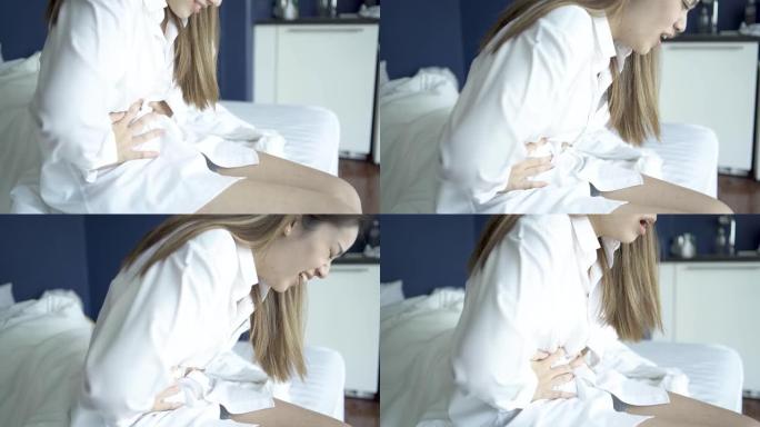 突然的女人有膀胱疼痛和胃痛坐在床上在卧室醒来后感到恶心和痛苦。