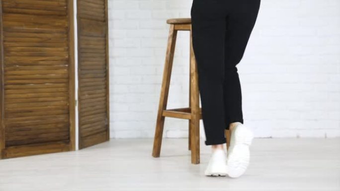 黑色牛仔裤模特展示白色大鞋。女士转身展示时髦的鞋子。背景下的木制塔布雷特。