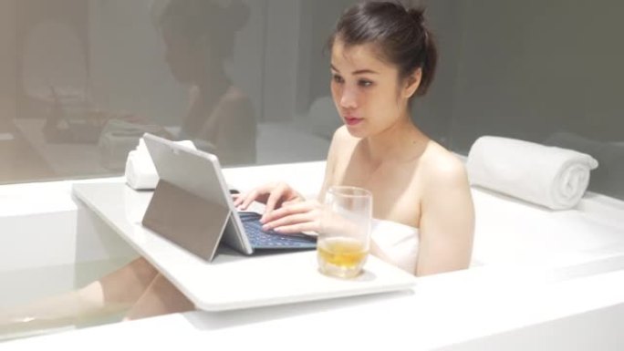 在浴缸里的平板电脑上在线工作的女商人。