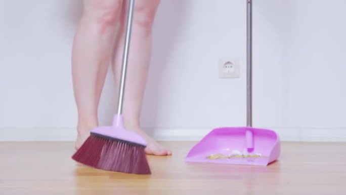 人打扫公寓，用一把长柄扫帚将垃圾扫成勺子，低角度视图。有家庭电话的清洁服务。打扫酒店房间。