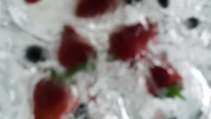男性的手将新鲜的浆果滴入水中，在厨房的烹饪过程中清洗甜草莓和蓝莓水下视图，自下而上，从下方慢动作视图