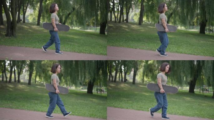 侧视图年轻的高加索美女，侏儒症，在公园里用滑板漫步。周末在户外慢动作行走的健康小人物的跟踪镜头。