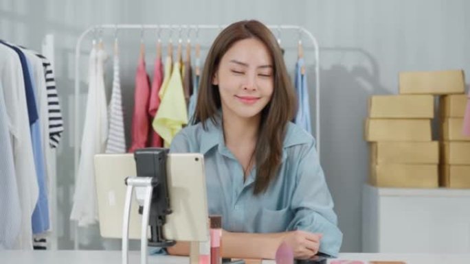 亚洲女性的肖像在网上卖服装，看着相机。迷人美丽的年轻女商人坐在桌子上，自信满满，对仓库中的金融业务感