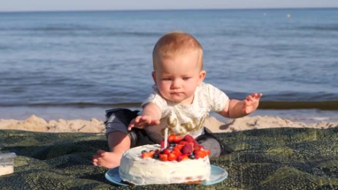 在海边为婴儿蹒跚学步的女孩庆祝一岁生日，地毯上放着甜蛋糕和蜡烛