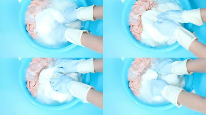 女性双手戴着橡胶手套在盆子里洗粉色衣服，俯视图