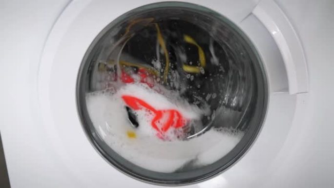 现代洗衣机用白色肥皂泡沫洗衣服。洗衣机里面装满了五颜六色的洗衣。旋转旋转滚筒洗衣机，特写