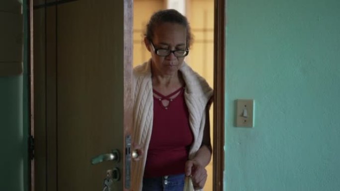 一位年长的妇女回家打开前门。人开门进入房子