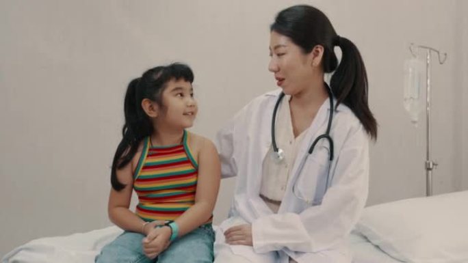 亚洲女孩医生拥抱并与病人在病房里的病床上交谈。快乐的孩子检查她的身体，坐在床上。儿童医疗保险，医学和