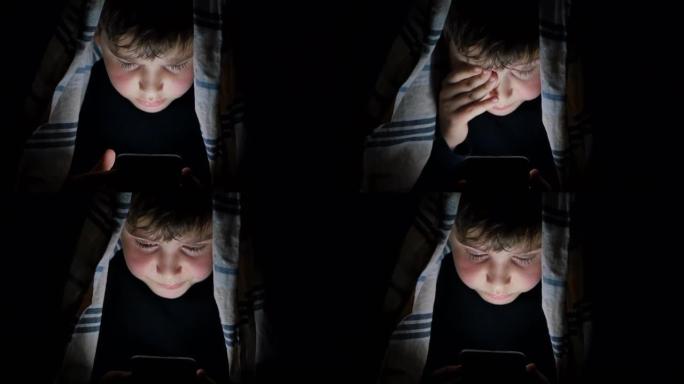 由于屏幕的影响和睡眠的欲望，一个十几岁的男孩在晚上使用智能手机偷偷浏览在线内容，躲在被窝下并用手揉眼