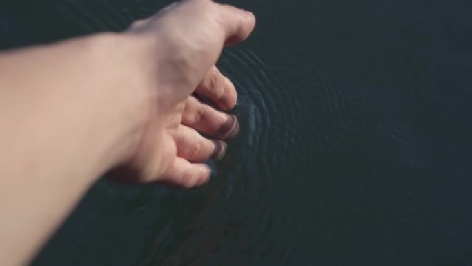 日落时分，雌性手浸入蓝色的水中，在河中流淌着波纹