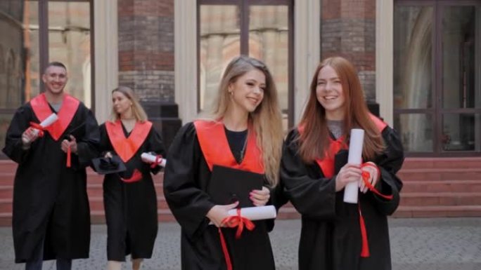 最好的女性开朗的朋友学生参加毕业典礼，穿着毕业礼服，穿着毕业礼服，拿着文凭，以高中大学教育理念为背景