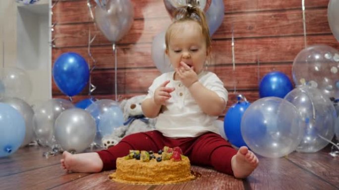 沾满食物的婴儿脸用手指吃一个甜蜜的生日蛋糕在地板上，浆果顶部庆祝1年