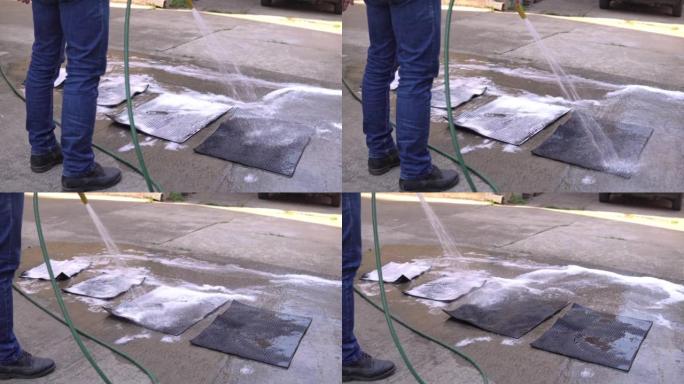 一名男子在后院洗汽车的汽车脚垫。
