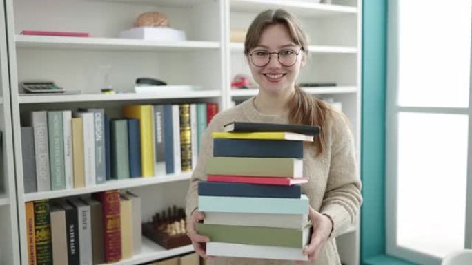 年轻的金发女子学生微笑着自信地拿着书在图书馆大学