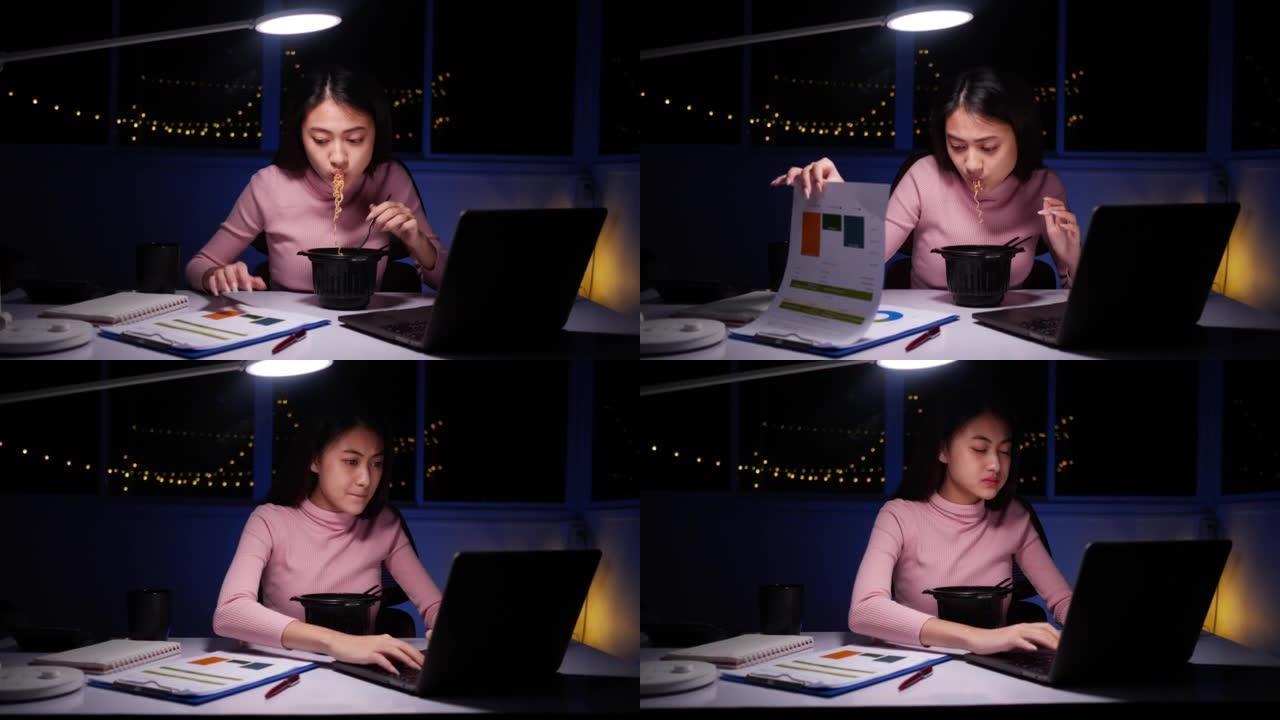 亚洲女商人在晚上在家笔记本电脑上工作时吃方便面