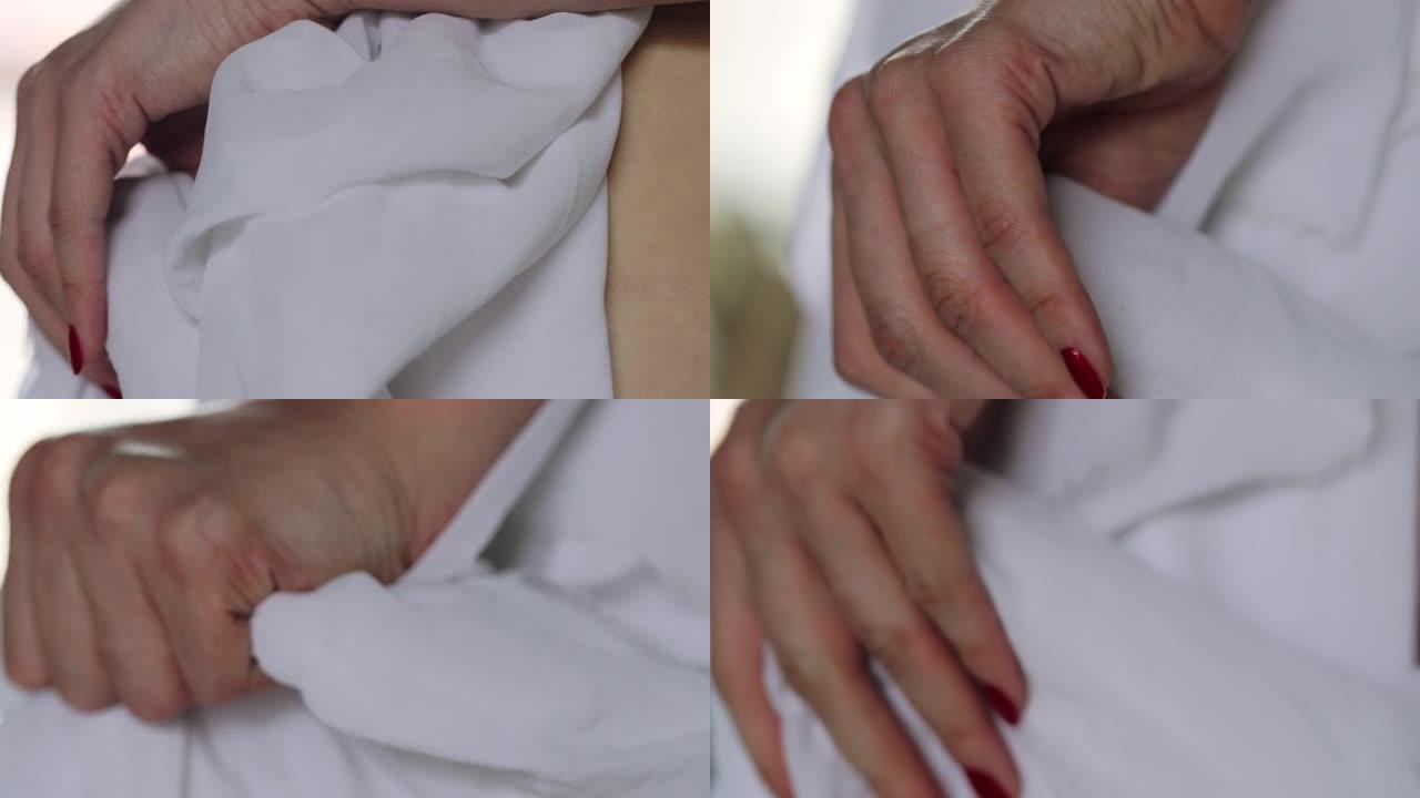 一个修指甲红色的女人的手用指甲夹住一块白布。女孩的手在手掌上性地握着一条丝绸毯子