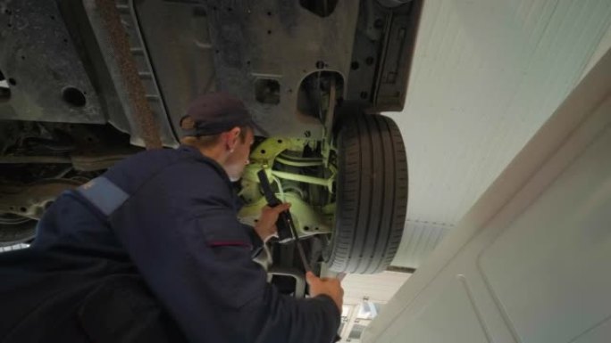 维修服务站的年轻汽车机械师检查举升汽车的车轮和悬架细节。底视图。