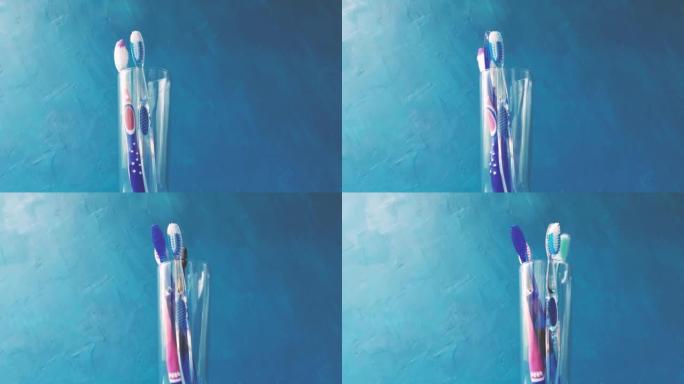 一只手将不同的多色牙刷放入蓝色背景上的玻璃特写镜头中。4k原始视频，摄像机运动流畅。