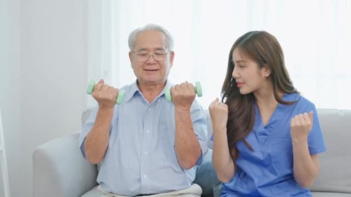 亚洲老年男子在护士的支持下进行物理治疗。老年成熟的男性患者坐在客厅的沙发上，在疗养院护理中与治疗师医