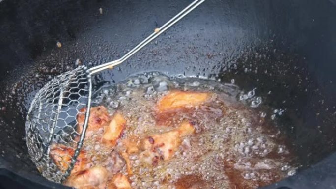 厨师正在在木头上的大锅中煎炸鸡翅，油正在沸腾