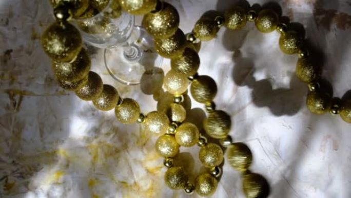 极简的节日抽象静物，酒杯和珠子作为豪华装饰，高对比度，阴影和阳光。金色