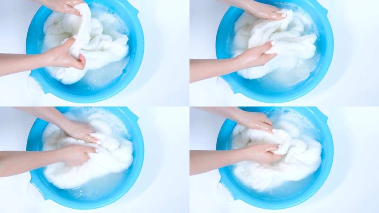 女性双手在盆子里洗白色毛巾，俯视图。