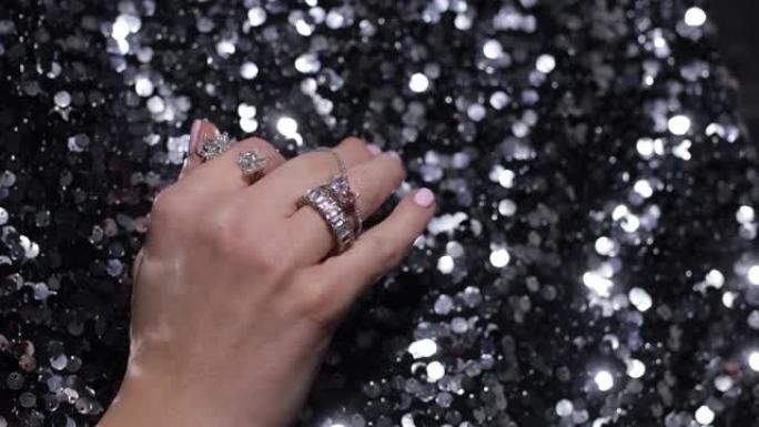 视频特写优雅的手移动手指与闪闪发光的宝石和珠宝戒指在黑色闪闪发光的纺织品背景。豪华丰富的配饰，银戒指