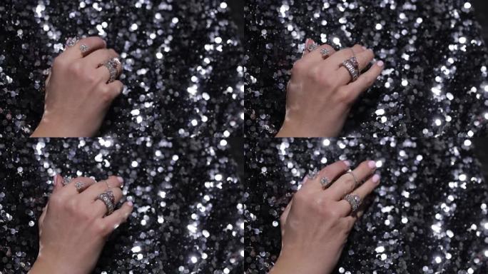 视频特写优雅的手移动手指与闪闪发光的宝石和珠宝戒指在黑色闪闪发光的纺织品背景。豪华丰富的配饰，银戒指