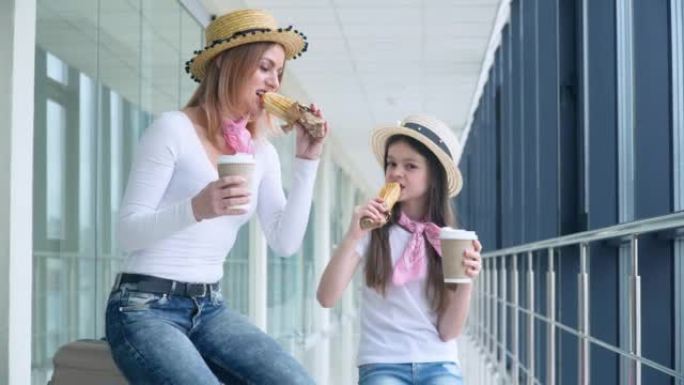 妈妈和女儿在机场等飞机时吃热狗和喝咖啡。航班延误