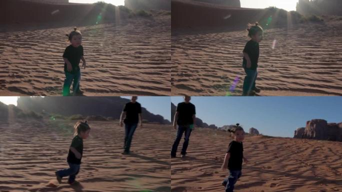 年轻的母亲和她蹒跚学步的儿子在亚利桑那州纪念碑谷的家附近的沙丘上玩耍和奔跑