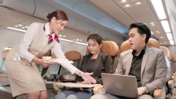 在飞机上，一位友好的亚洲女空姐在与顾客交谈的同时提供食物和饮料。提供航空服务。