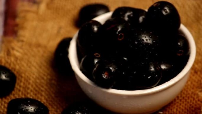 带有水滴的越橘，木质背景上的黑色jamun水果，新鲜成熟的甜蓝莓覆盖着水滴