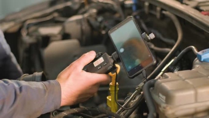 汽车修理工的手用带有旋转摄像头和手机的技术内窥镜检查车辆发动机。修理发动机头和气门。
