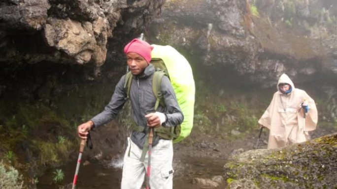 徒步旅行者带着背包和登山杖行走，同时徒步穿越乞力马扎罗山经过瀑布