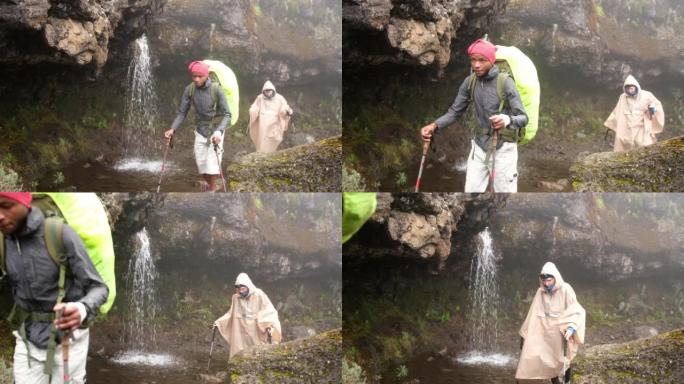 徒步旅行者带着背包和登山杖行走，同时徒步穿越乞力马扎罗山经过瀑布