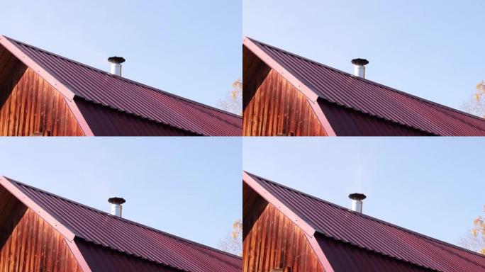 居民楼红色屋顶上的烟囱冒出淡淡的烟雾，与一棵秋树的蓝天和树枝相抵。